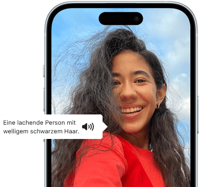 Ein iPhone 15 mit dem Feature VoiceOver, das eine Bildbeschreibung liefert: lachende Person mit welligem schwarzem Haar